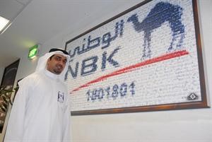 احد موظفي البنك امام لوحة تضم صور موظفي الوطني التي ترمز لشعاره﻿