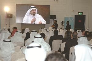 الشيخ خليفةالعلي معترضا على انعقاد الجمعية العمومية كما يبدو على شاشة في القاعة الثانية