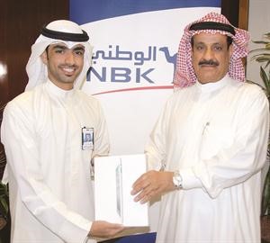 الفائز غنيم ادهام غنيم الزيد يتسلم الجائزة من مسؤول العلاقات العامة لدى الوطني يعقوب الباقر﻿