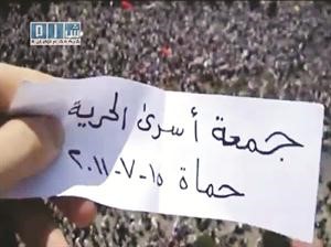 صورة عن الانترنت لمتظاهر يصور الحشود في حماة ويحمل ورقة بتاريخ جمعة اسرى الحرية	افپ﻿