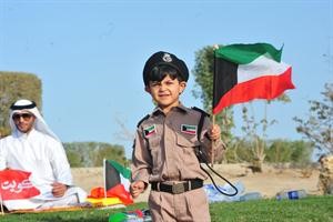 طفل بالزي العسكري يحمل علم الكويت