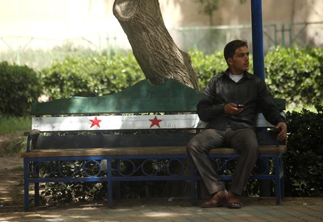 مواطن سوري يجلس على كرسي في حديقة مرسوم عليه علم الثورة السورية في مدينة الرقة افب