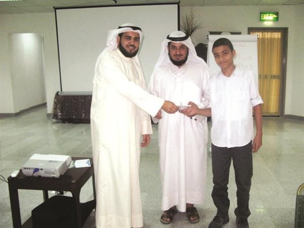 احد طلاب مدرسة ملا عيسى ينوب عن زملائه بتسليم تبرع لمشروع الدينارين بالهيئة الخيرية ﻿