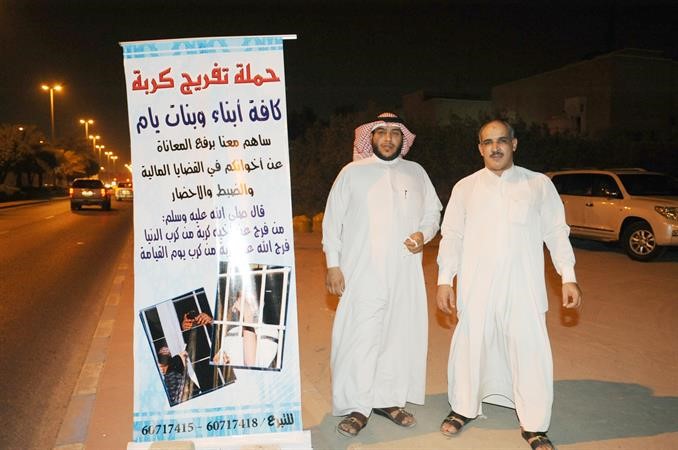 مشرف الحملة ثفنان العجمي بجوار بوستر لدعوة المواطنين للتبرع لمساعدة المكروبين﻿