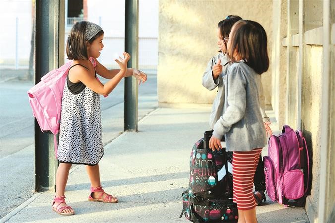 طفلة في المدرسة تتحدث مع زميلتيها بلغة الاشارة ﻿
