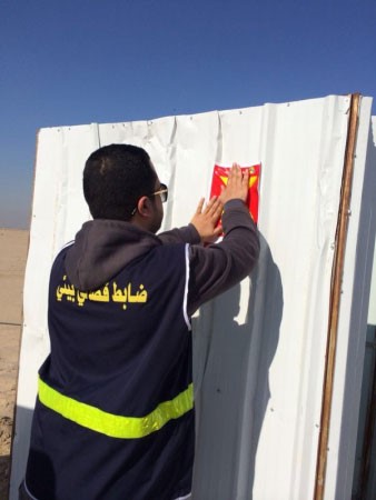 احد اعضاء فريق التفتيش يضع ملصقا تحذيريا﻿