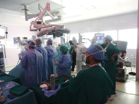 الروبوت فوق المريض مع المساعد السريري والممرض ويظهر برج التحكم من اليمين الى اليسار