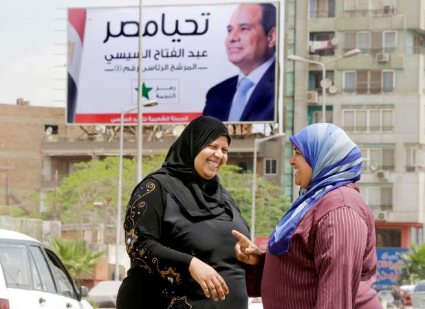 مصريتان تتحدثان بالقرب من لوحة تدعم المشير السيسي في الانتخابات الرئاسية في القاهرة امس 	افپ﻿