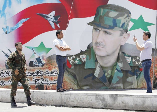 صورة تذكارية لسوري بجانب لافتة عملاقة داعمة للرئيس بشار الاسد في دمشق افپ