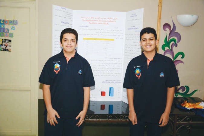 الطالبان عبدالله الاشوك وناصر المشعل امام لوحة عرض مشروعهما ﻿
