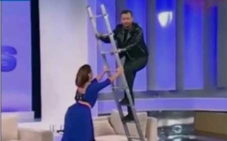 بالفيديو.. مذيع يسقط من أعلى سلم حديدي على الهواء ويقع على زميلتيه