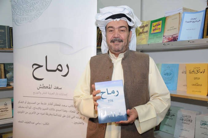 المعطش يحمل نسخة من كتابه رماح بينما تبدو اشادة الزميل سامي النصف على البوستر﻿