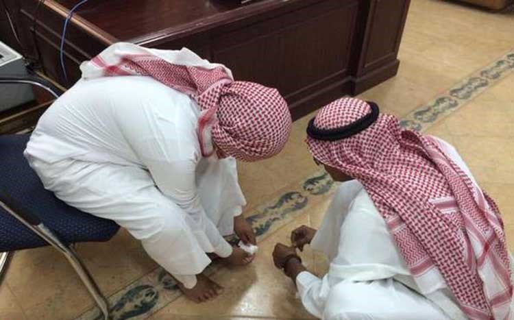 بالصور.. معلم على الأرض ويجلس أحد طلابه على كرسي لتضميد جرح بقدمه