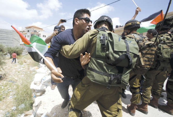 شاب فلسطيني يدفع جنود الاحتلال خلال مظاهرة ضد الاستيطانبالضفة الغربية امسرويترز ﻿