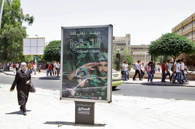سيدة سورية خلال مرورها امس بجوار لوحة اعلانية باحد شوارع دمشق تحث الشباب على الانضمام للجيش افپ

