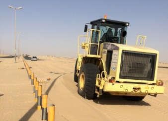 احدى اليات البلدية تقوم بازالة الرمال من الطريق﻿