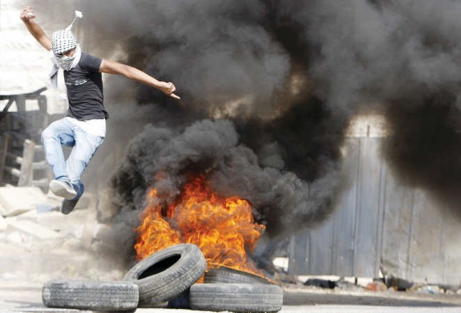 متظاهر فلسطيني يقفز فوق الاطارات التي اشعلها محتجون في الخليل بالضفة الغربية امس الاول	رويترز ﻿