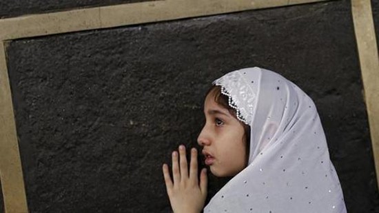 صورة لطفلة تتعلق بأسوار الكعبة محاولة احتضانها
