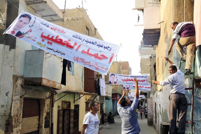مصريون يقومون بتعليق دعاية انتخابية لاحد مرشحي مجلس النواب في دائرة الدقي امس 	رويترز﻿