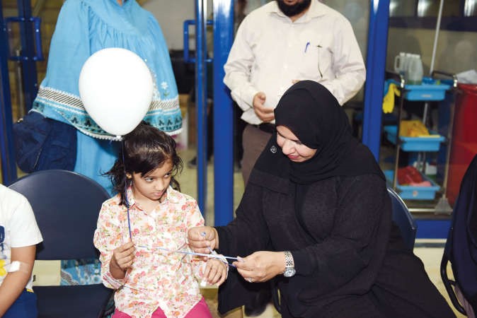 المطيري تساعد احدى الاطفال في ربط بلونتها