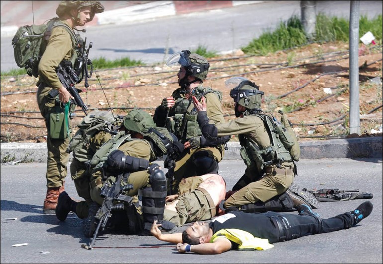 جنود اسرائيليون يتجمعون حول جثة زميلهم وبجوارهم جثمان الشهيد الفلسطيني الذي طعنه في الخليلاپ
