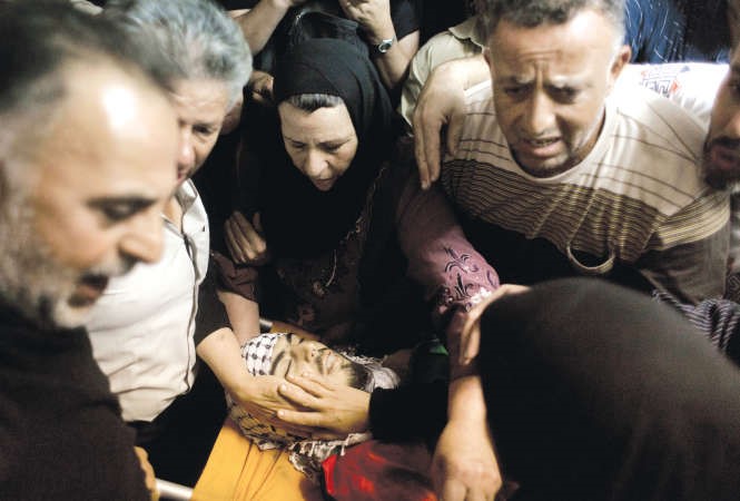 ام احد الشهداء الفلسطينيين الذي سقط خلال اشتباكات مع القوات الاسرائيلية امس الاول تلقي النظرة الاخيرة على جثمان ابنها قبل دفنه امسوفي الاطار مستوطن يهودي يحمل سلاحا ويشير الى جثة فلسطيني قتله وبجواره جنود الاحتلال امسافپ - رويترز﻿
