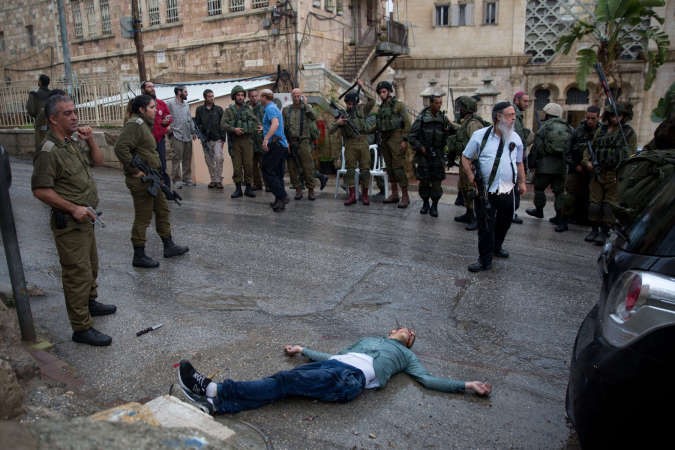 جنود ومستوطنون اسرائيليون يتجمعون حول جثة فلسطيني عقب قتله في مستوطنة بيت هداسا في الخليل بزعم محاولته طعن اسرائيلي 	افپ﻿