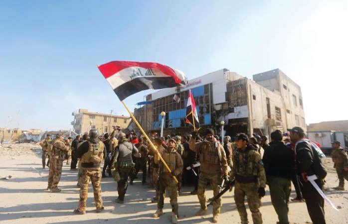 جنود عراقيون يلوحون بالعلم الوطني من امام مقر شرطة الانبار عقب تحريرهم مدينة الرمادي من ايدي داعش امس افپ
