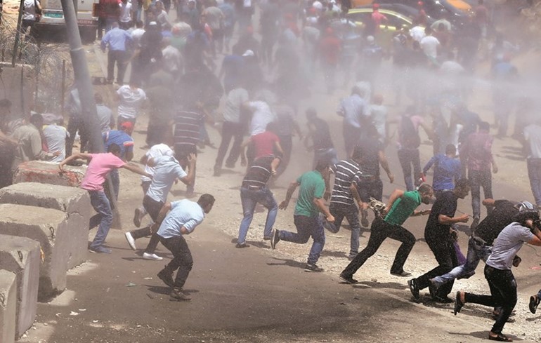 فلسطينيون يقاومون خراطيم المياه التي استخدمتها شرطة الاحتلال خلال مواجهات معهم عند حاجز قلنديا امس 	افپ﻿