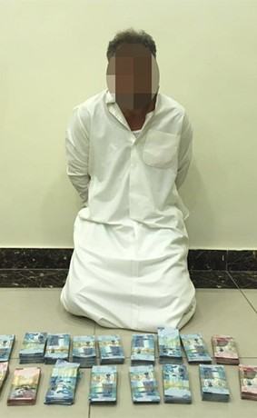 المتهم وأمامه المبالغ المسروقة