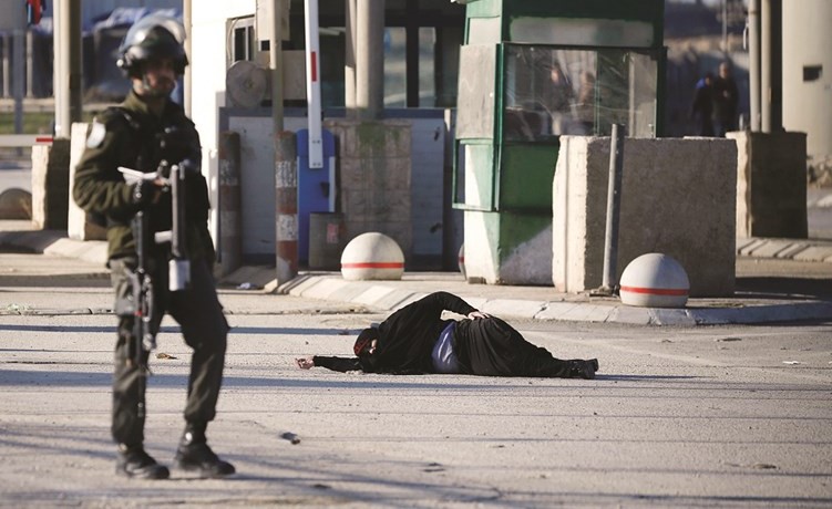 الفلسطينية الجريحة برصاص الاحتلال ممدة على الارض بعد اصابتها فيما يقف جندي اسرائيلي غيرمكترث بالقرب منها(ا.ف.پ)﻿