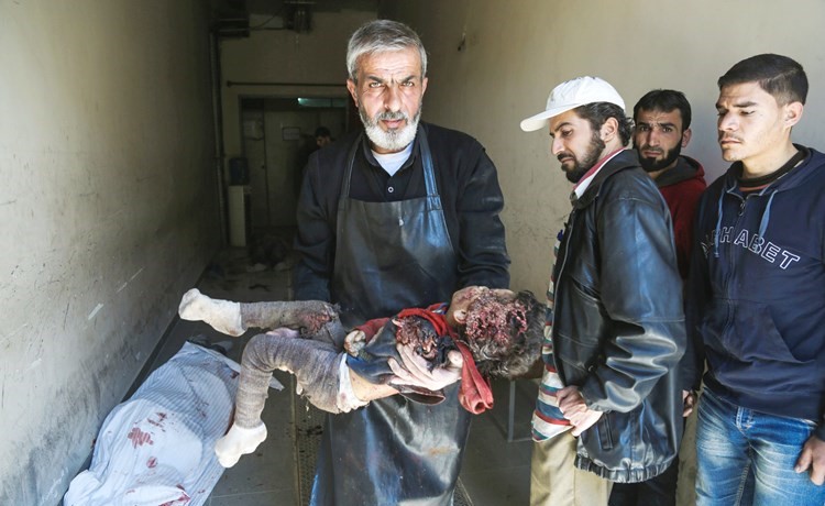 رجل يحمل جثة طفل قتل في غارة جوية على بلدة حمورية التي تسيطر عليها المعارضة بريف دمشق	(أ.ف.پ)﻿