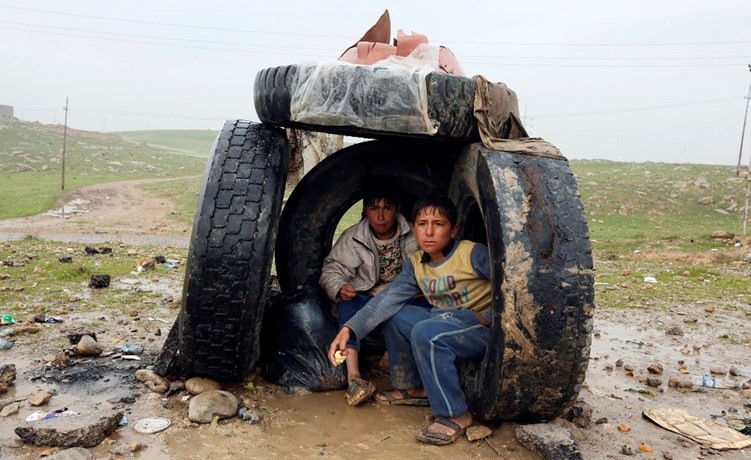 طفلان عراقيان يحتميان من المطر بإطارات سيارات قرب الموصل( رويترز) ﻿