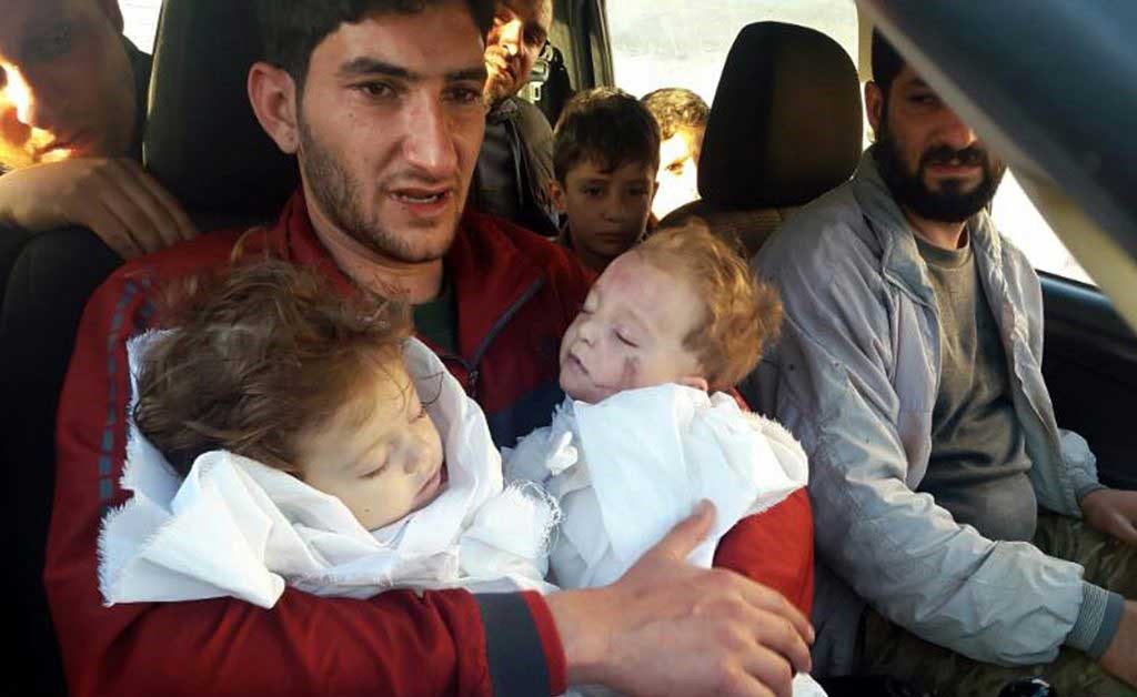صور مؤلمة.. سوري يحتضن جثماني توأمه بعد مجزرة إدلب