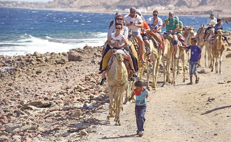 لقطة تظهر فوجا سياحيا يضم مصريين خلال الاستمتاع بركوب الجمال على شواطئ دهب بسيناء (أ.ف.پ)﻿