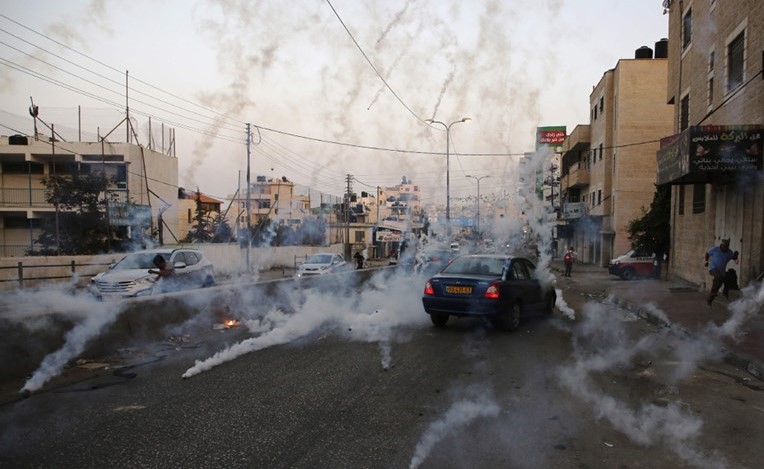 فلسطينيون يحتمون من دخان القنابل المسيلة للدموع التي اطلقها الاحتلال خلال مواجهات في قلنديا امس(ا.ف.ب) ﻿