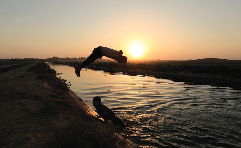 اطفال فارون من مناطق سيطرة «داعش» يسبحون في قناة للري بالرقة	(رويترز)
