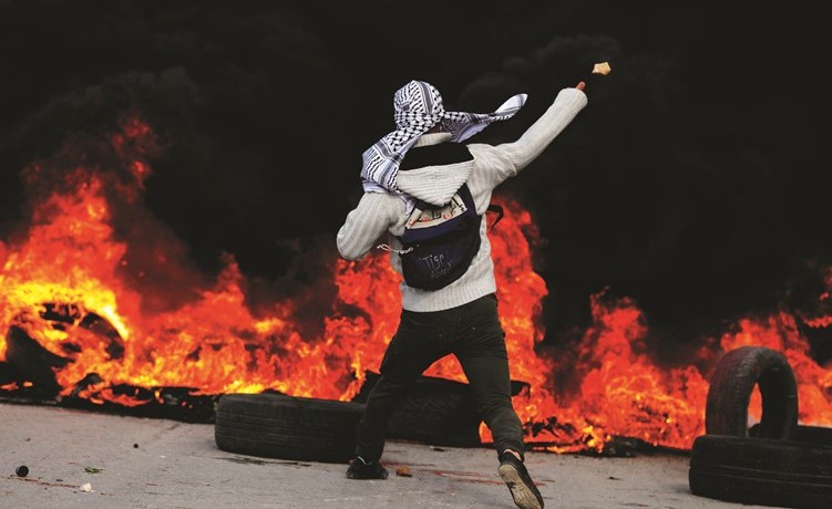 فلسطيني يرمي جنود الاحتلال بالحجارة في رام الله وسط الاطارات المشتعلة(رويترز) ﻿