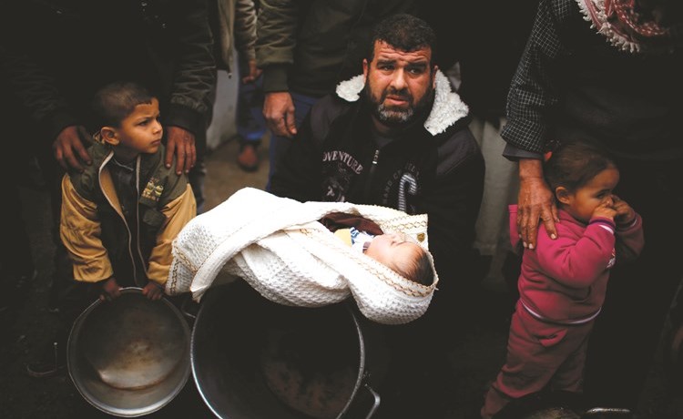 فلسطيني يحمل رضيعا والى جواره اطفال يمسكون بأوان فارغة احتجاجا على تجميد المساعدات الامريكية في غزة امس	(رويترز) ﻿