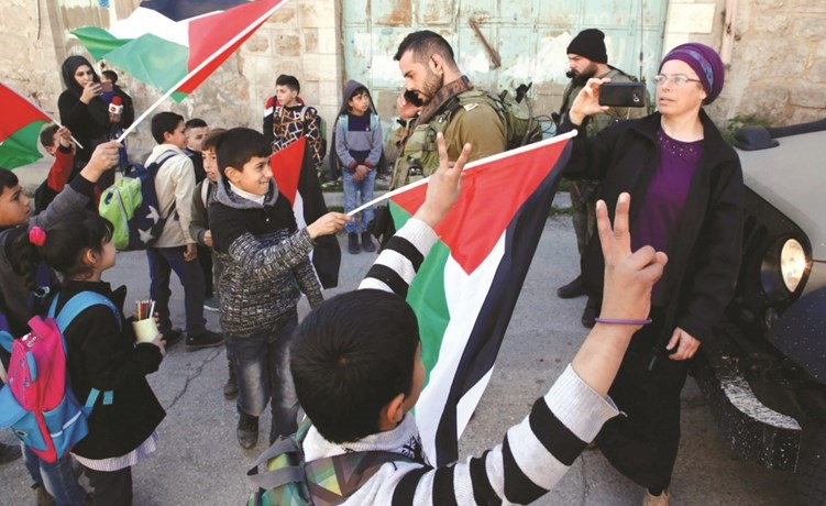 أطفال فلسطينيون يلوحون بالأعلام الوطنية في وجه جنود الاحتلال في احد شوارع الخليل أمس	(أ.ف.پ) ﻿
