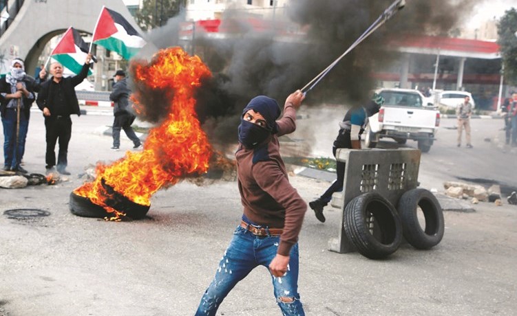 فلسطيني يلقي بالحجارة باتجاه قوات الاحتلال فيما بدا اخرون يلوحون بعلم فلسطين خلال مواجهات قرب رام الله امس الاول	(أ.ف.پ)﻿