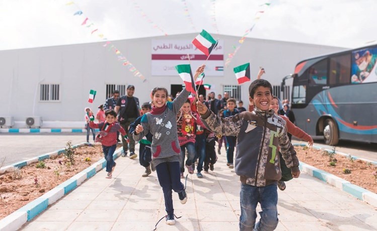 عدد من الاطفال السوريين يحملون علم الكويت ﻿