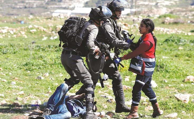 جنديان اسرائيليان يمنعان مسعفة من تقديم العلاج لأحد المصابين في مواجهات قرب رام الله امس (رويترز) ﻿
