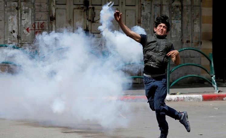 شاب فلسطيني يعيد القاء قنبلة مسيلة للدموع باتجاه قوات الاحتلال خلال مواجهات في الخليل امس ( رويترز) ﻿