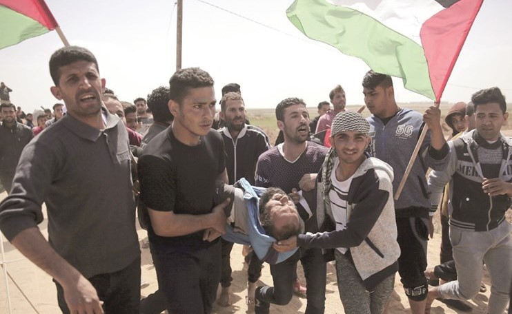 فلسطينيون يحملون مصابا برصاص الاحتلال خلال مواجهات على حدود غزة امس	(ا.پ)﻿