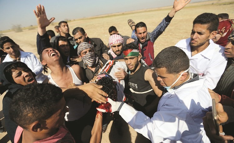 فلسطينيون يحملون شابا مصابا خلال مواجهات مع قوات الاحتلال على حدود غزة امس       (رويترز) ﻿
