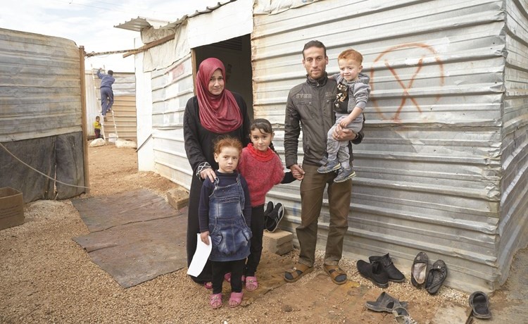 اللاجئة عائشة وابنتاها أروى وفاطمة مع زوجها غريب وابنها عماد خارج ملجئهم في مخيم الزعتري ﻿