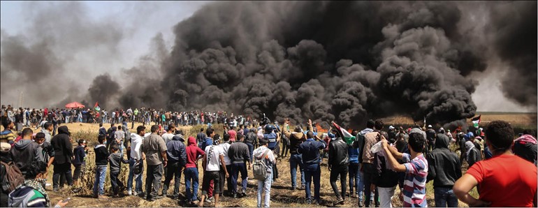 فلسطينيون يلوحون بعلم بلادهم فيما الدخان الأسود الناتج عن حرقهم «الكاوتشوك» يتصاعد باتجاه قوات الاحتلال على السياج الحدودي لقطاع غزة أمس 	(ا.ف.پ)