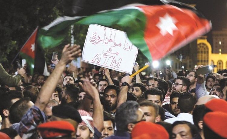 أردنيون يلوحون بعلم بلادهم ويرفعون لافتة رافضة لمشروع قانون الضريبة خلال تظاهرة بعمان مساء امس الأول 	(أ.ف.پ)﻿
