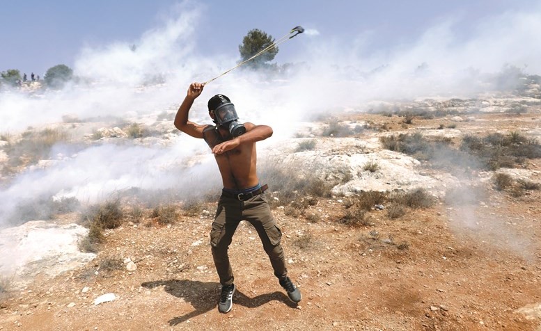 متظاهر فلسطيني يلقي الحجارة على قوات الاحتلال خلال مظاهرة ضد بناء المستوطنات الإسرائيلية قرب رام الله	(رويترز)﻿